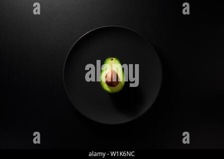 One avocado slice with kernel served in black plate on moody black background. Top view. Healthy diet concept. Stock Photo