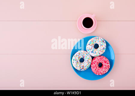 Donuts or doughnuts in a turquoise plate with espresso cup on pink wooden table background with copy space. Top view. Stock Photo