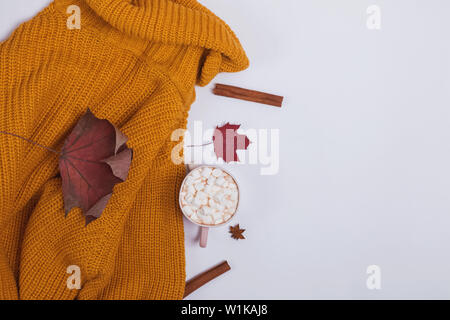 Creative autumn composition with warm knitted sweater, yllow leaves and cocoa with marshmllows on the white background, top view Stock Photo