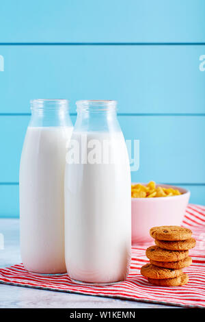 Milk bottles, chocolate chip cookies and a bowl of cereal on wooden table with turquoise wooden background Stock Photo