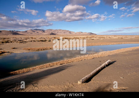 Arare stream winds through Utah's West Desert with dry mud caked along its shoreline and puffy clouds high above a nearby mountain range, west of Salt Stock Photo