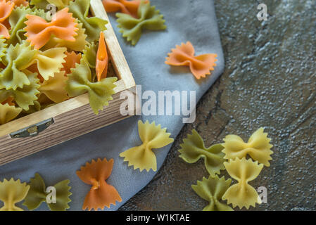 Colorful pasta bow ties in a wooden box on a rustic background Stock Photo