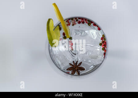 Gin Tonic in a glass cup with some slices of lime and lemon,pink pepper and anise on a white background Stock Photo