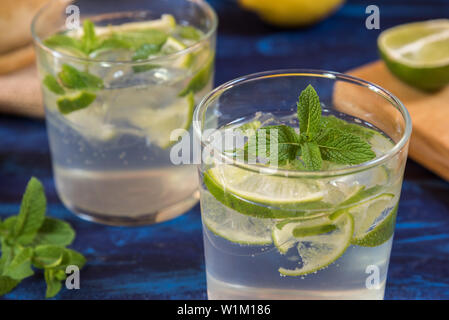 Mojito cocktail on a blue table with its peppermint,lemon and lime ingredients Stock Photo