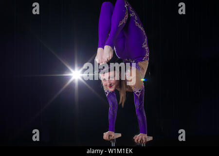 Circus actress performs the number in a beautiful smoke. Manual equilibrium on canes. Flexible girl body.Performance of an air gymnast in a circus Stock Photo