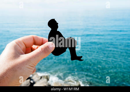 closeup of the hand of a man with a black paper cutout in the shape of a man cannonballing into the ocean Stock Photo