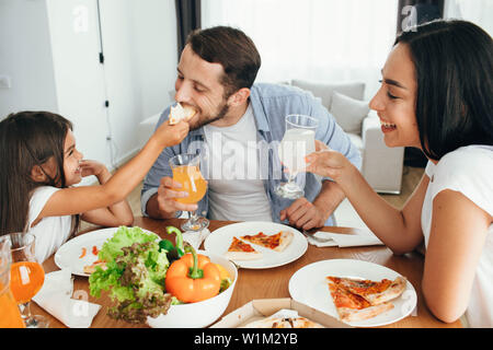 Family enjoying pizza lunch. Father, mother and daughter during dinner.Yammy, it's very tasty piece of pizza Stock Photo
