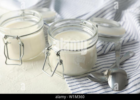 https://l450v.alamy.com/450v/w1m360/glass-jars-with-sour-cream-yogurt-spoons-and-towel-on-white-cement-background-w1m360.jpg