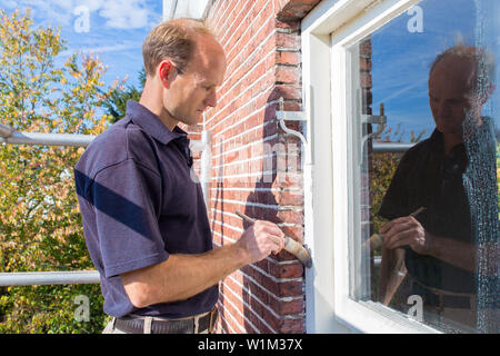 Caucasian painter painting window frame in facade of house with brush Stock Photo