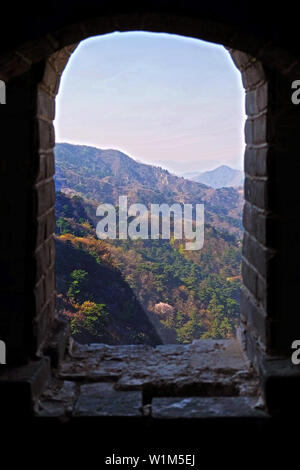 Panoramic view from the window of a watch tower of the Mutianyu section of the Great Wall of China, over the surrounding valley with green and yellow Stock Photo