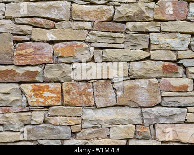The laying of the stone wall of wild stone collected in the mountains. Fragment of a stone wall as a texture or background. The wall of a typical buil Stock Photo