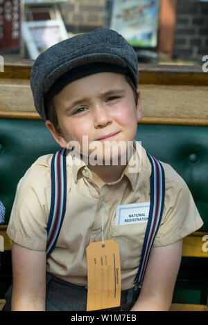 Kidderminster, UK. 29th June, 2019. Severn Valley Railways 'Step back to the 1940's' gets off to a fabulous start this summer weekend with costumed re-enactors providing an authentic recreation of WWII wartime Britain. Anxious, young evacuee boy, wearing braces, flat cap and name tag, sits isolated waiting at a vintage heritage railway station ready for the journey to his temporary new home in the countryside during these difficult times. Credit: Lee Hudson Stock Photo