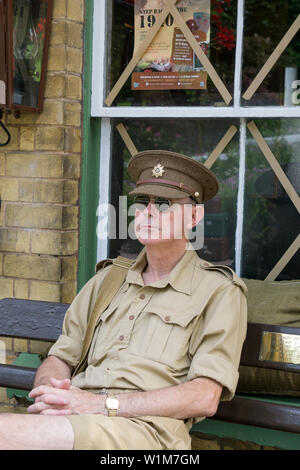 Kidderminster, UK. 29th June, 2019. Severn Valley Railways 'Step back to the 1940's' gets off to a fabulous start this weekend with costumed re-enactors playing their part in providing an authentic recreation of wartime Britain. Isolated man in army khaki uniform sits on a bench at a vintage railway station patiently awaiting the arrival of the next steam train. Credit: Lee Hudson Stock Photo