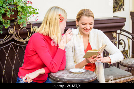 Discussing popular bestseller book. Female literature. Book every girl should read. Girls friends sitting cafe terrace drinking coffee. Reading inspiring book. Self improvement and education. Stock Photo