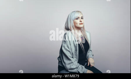 Side view of a fashionable woman in white hair looking at camera. Woman with fashion piercing on cheeks isolated on grey background. Stock Photo
