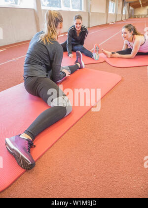Three young women practicing yoga in athletics hall on tartan track, Offenburg, Baden-Württemberg, Germany Stock Photo