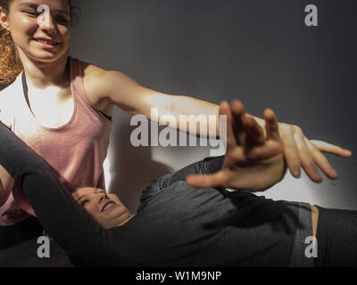 Fitness instructor helping young woman doing physical therapy in athletics hall, Offenburg, Baden-Württemberg, Germany Stock Photo