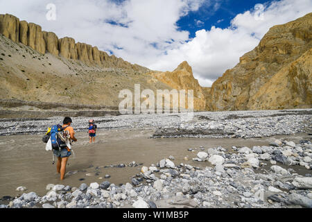 Two young men, hiker, trekker crossing the river Dhechyang Khola in the surreal landscape typical for Mustang in the high desert around the Kali Ganda Stock Photo