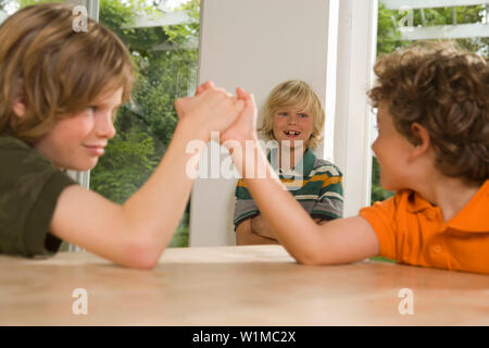 Two boys arm wrestling, one boy standing in background, children's birthday party Stock Photo