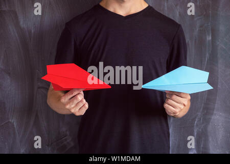 Man holding two paper planes in his hands. One of them is red, the other is blue. Close up. Stock Photo