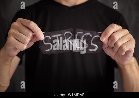 Man ripping Stress word written on black paper. Close up. Stock Photo