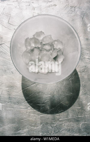 Glass plate with ice. Large ice cubes on a gray textural background. Hard shadow from the sun. Natural daylight from the window falls on a transparent Stock Photo