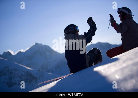 Young man and woman sitting on snow, clapping hands, Kuehtai, Tyrol, Austria Stock Photo
