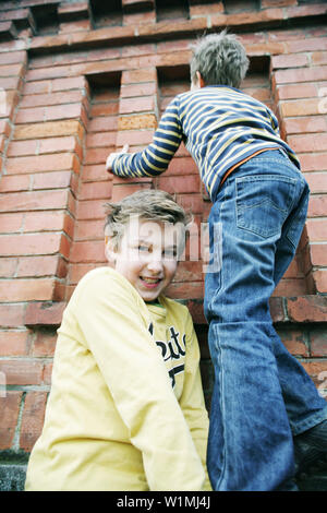 Boy giving friend a bunk-up over a wall Stock Photo