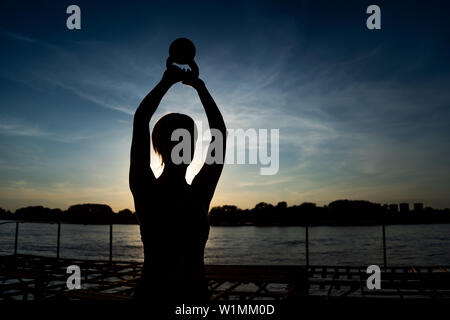 Woman exercising pilates with kettlebell in sunset. Stock Photo
