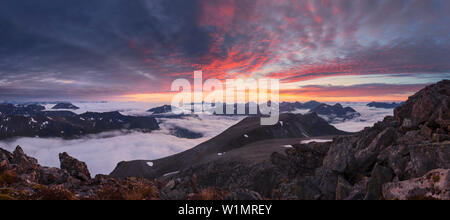 Wide view from top of Skårasalen (1542m) with an impressive sunset over the clouds and the mountains of the Sunnmøre Alps with rocks in foreground, Mø Stock Photo