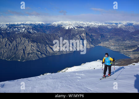 Female back-country skier ascending to Monte Baldo, lake Garda in background, Monte Baldo, Garda Mountains, Trentino, Italy Stock Photo