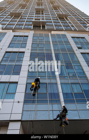 Cleaning windows on a high rise building using ropes and abseiling equipment on Al Reem Island in Abu Dhabi, UAE Stock Photo