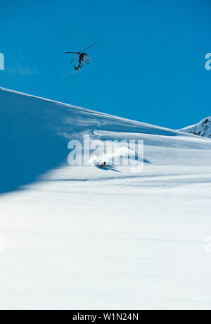 Skier downhill skiing in deep snow, helicopter in background, Chugach Powder Guides, Girdwood, Alaska, USA Stock Photo