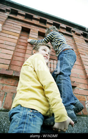 Boy giving friend a bunk-up over a wall Stock Photo