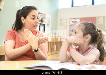 Sign language teacher in a extra tutoring class with a deaf child girl using American Sign Language. Stock Photo
