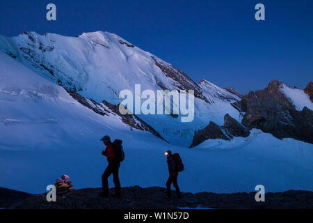 A man and a woman hiking with head torches, ascent at dawn to the summit of Mount Wildi Frau, view towards Bluemlisalp mountains, Bluemlisalphorn, Ber Stock Photo