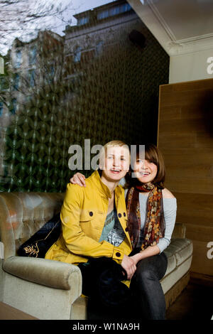 Two young woman sitting on a sofa while looking out of a window Stock Photo