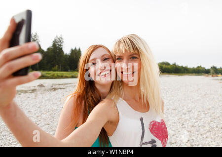Two young women taking pictures of themselves by a mobile phone, Munich, Bavaria, Germany Stock Photo