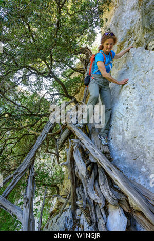 Woman hiking Selvaggio Blu climbing down over juniper branches, Selvaggio Blu, National Park of the Bay of Orosei and Gennargentu, Sardinia, Italy Stock Photo