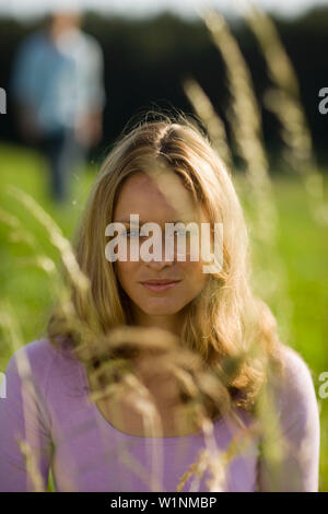 Young woman sitting on meadow, unrecognizable person in background Stock Photo