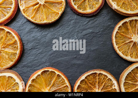Bright slices of dried orange on a black slate texture board background, copy space. Stock Photo
