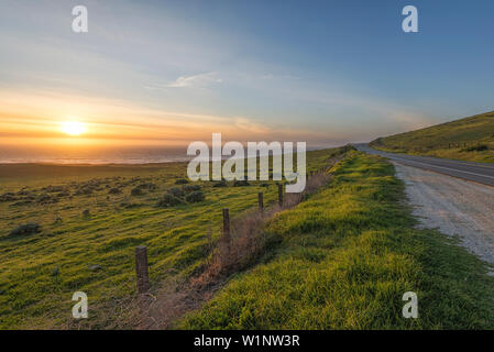 The Sun setting over the ocean with a meadow in the foreground. Big Sur, California, United States. Stock Photo