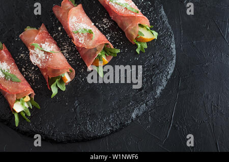 Prosciutto rolls stuffed with arugula and pears on black slate. Stock Photo