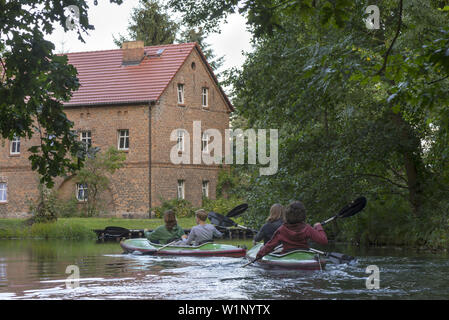 Kayak tourists paddling through a village and passing by a brick house, biosphere reserve, Schlepzig, Brandenburg, Germany Stock Photo