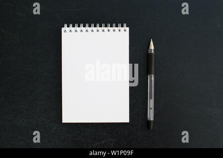 Open a blank notepad on the spiral on a black board background with black pen. Stock Photo