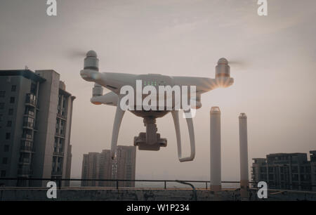 Back view of white quadcopter drone with attached camera filming at golden light. Stock Photo