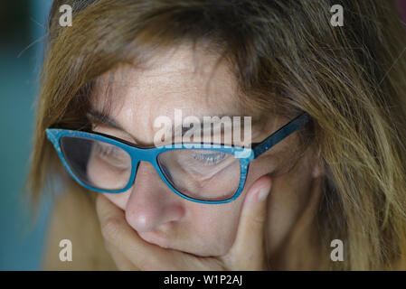 Portrait of stressed mature woman with hand on mouth looking down, close up. Computer monitor light reflection on face. Worried woman wearing eyeglass Stock Photo