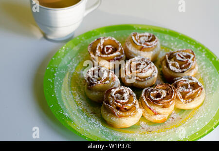 Homemade cookies roses with a sugar powder on colorful plate and a latte cup. Breakfast and dessert concept. Stock Photo