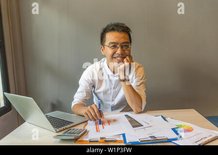Smiling young businessman sitting at workplace with documents and laptop Stock Photo