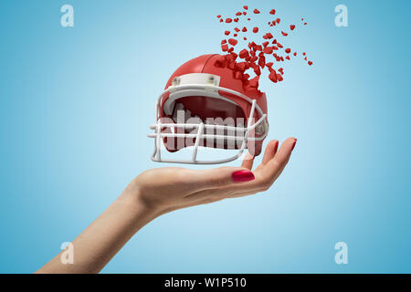 Closeup of woman's hand holding sports helmet which is breaking into small pieces that are flying away on light blue background. Stock Photo